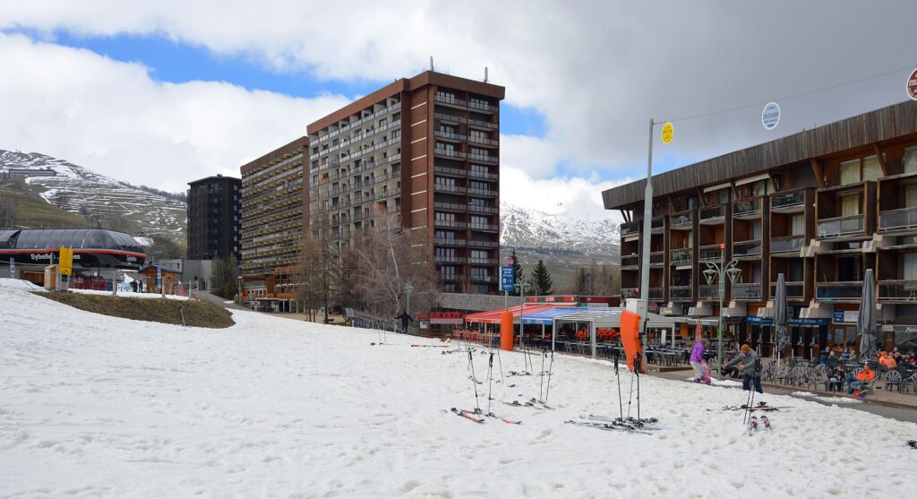 Skis planted in the snow on the snow front at Le Corbier, with the resort's apartment buildings and cafés behind