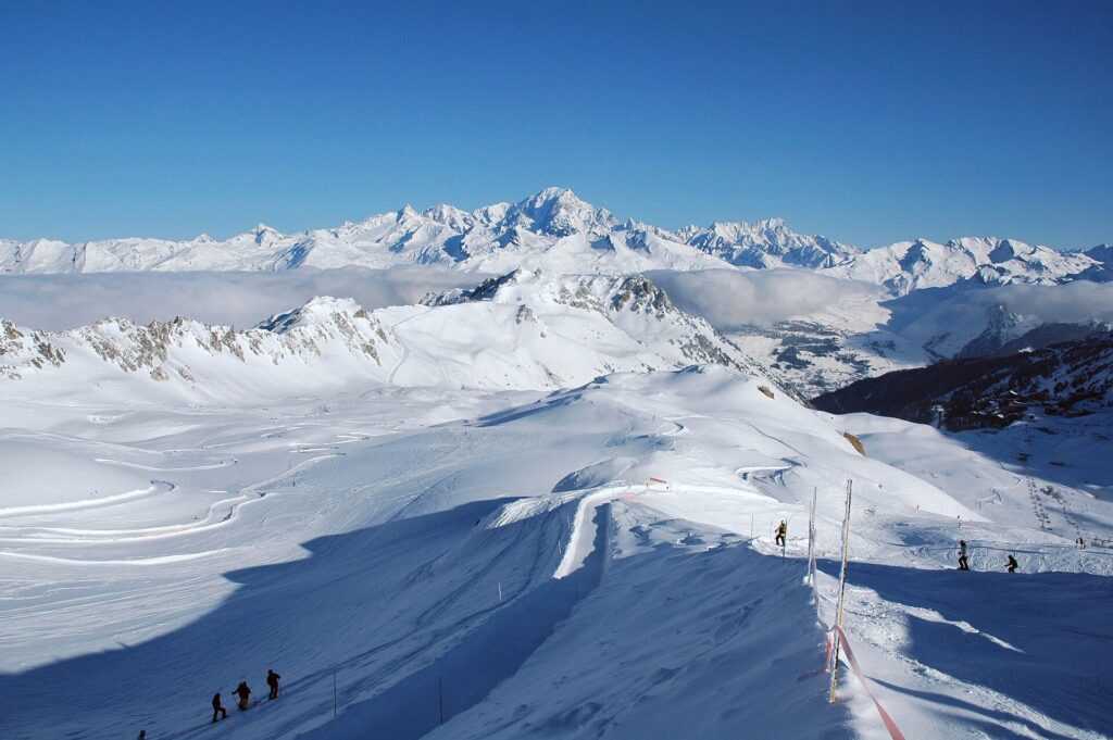 Skiers on a ridge-top piste with a long view of Alpine peaks