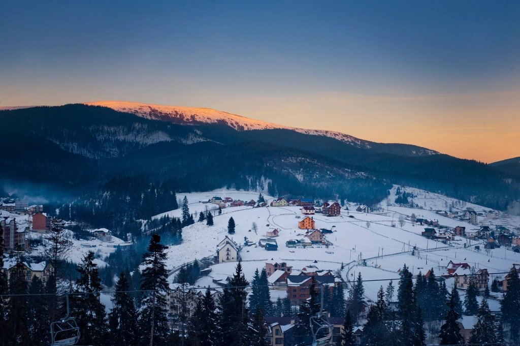 Snowy ski village in a forested valley at dusk